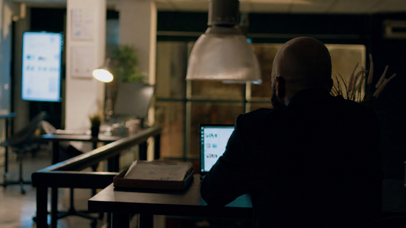 A bald entrepreneur working alone at a laptop late at night, representing the years Russelle Avionn spent building Avionn Automotive after work.